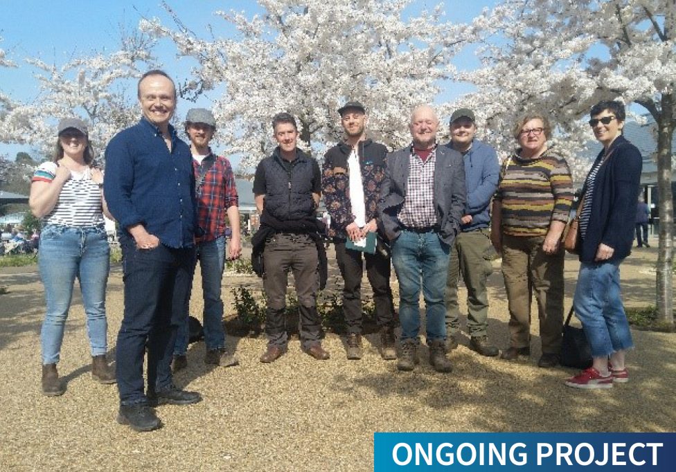 Flood Innovation Centre staff and community garden group members in front of flowering cherry trees with the text "Ongoing Project"