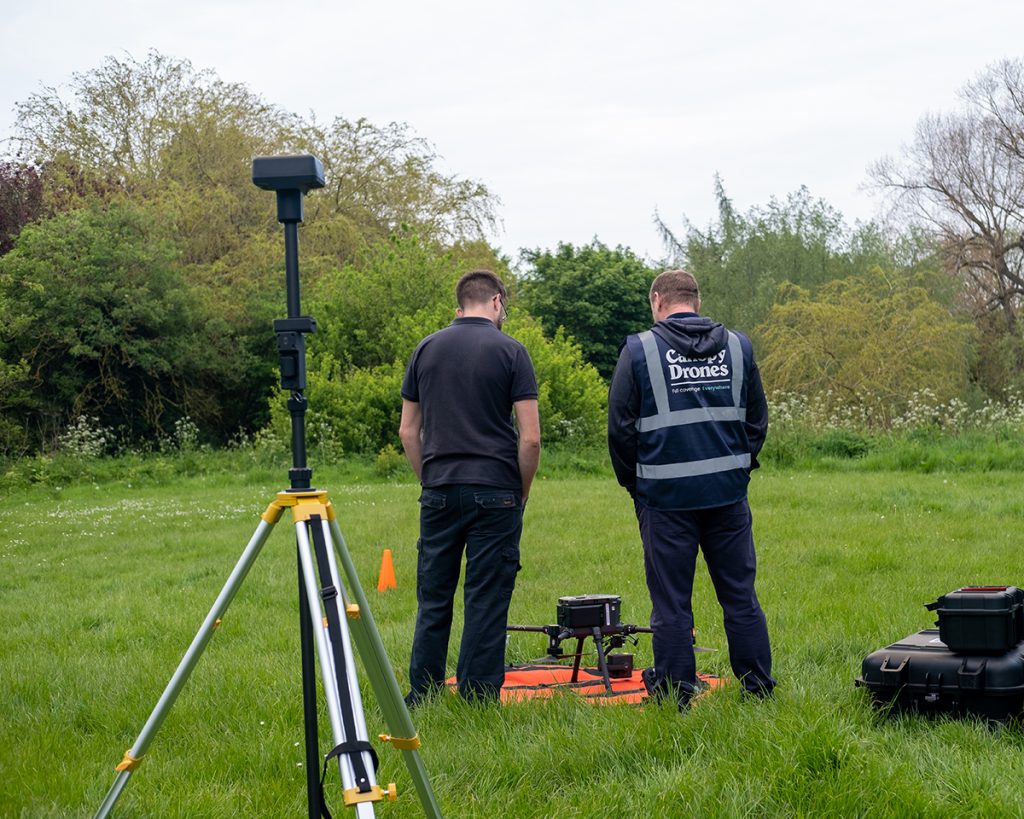 The Canopy Drones team set up their drone equipment in a green field, surrounded by hedges 